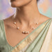 A delicate gold chain necklace displayed on a light gray fabric jewelry bust. The necklace features five white pearls spaced along the chain, with a central gold bead embellished with tiny clear stones.